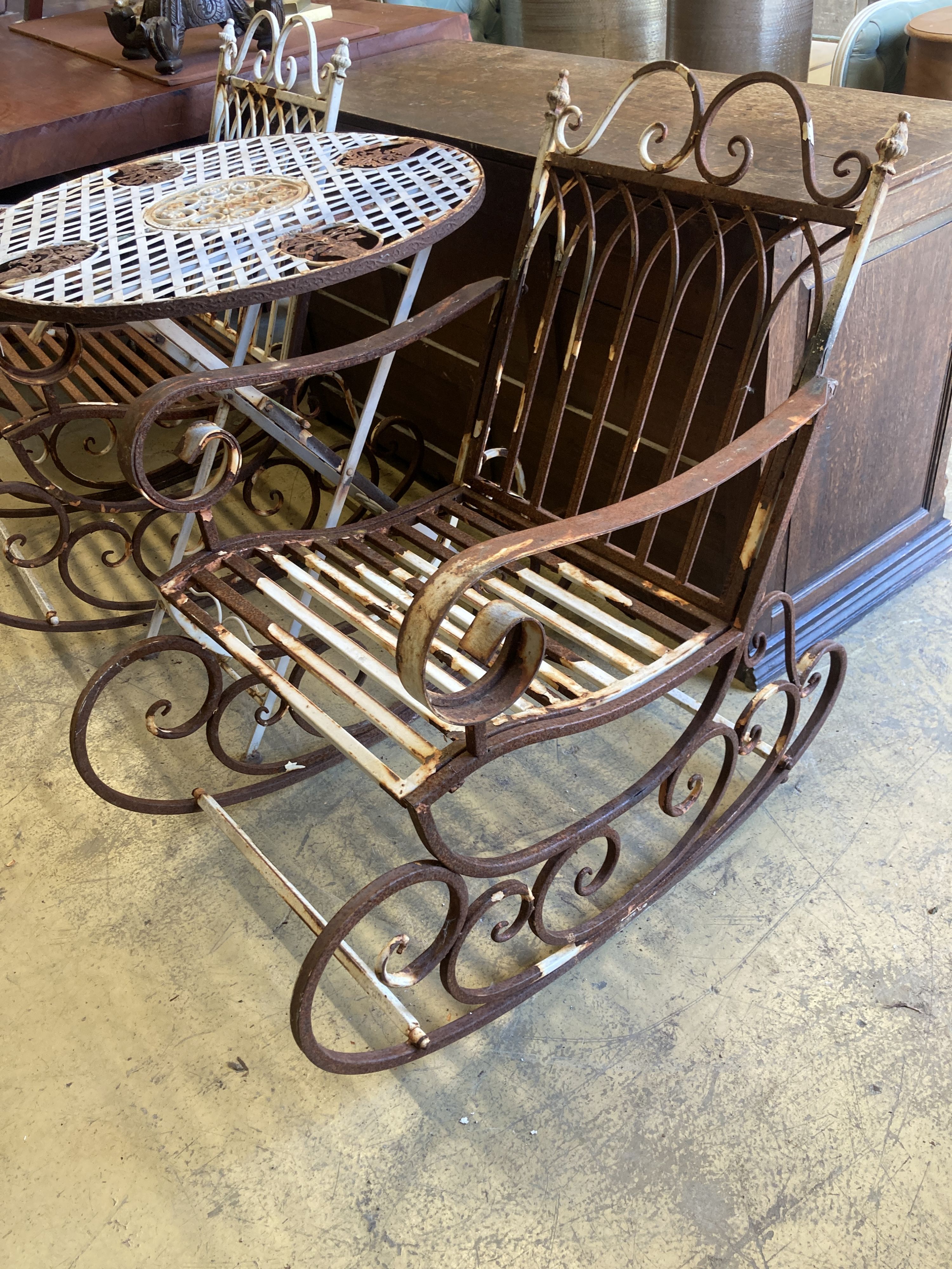 A pair of painted wrought iron garden rocking chairs together with a circular wrought iron folding garden table, diameter 71cm, height 76cm